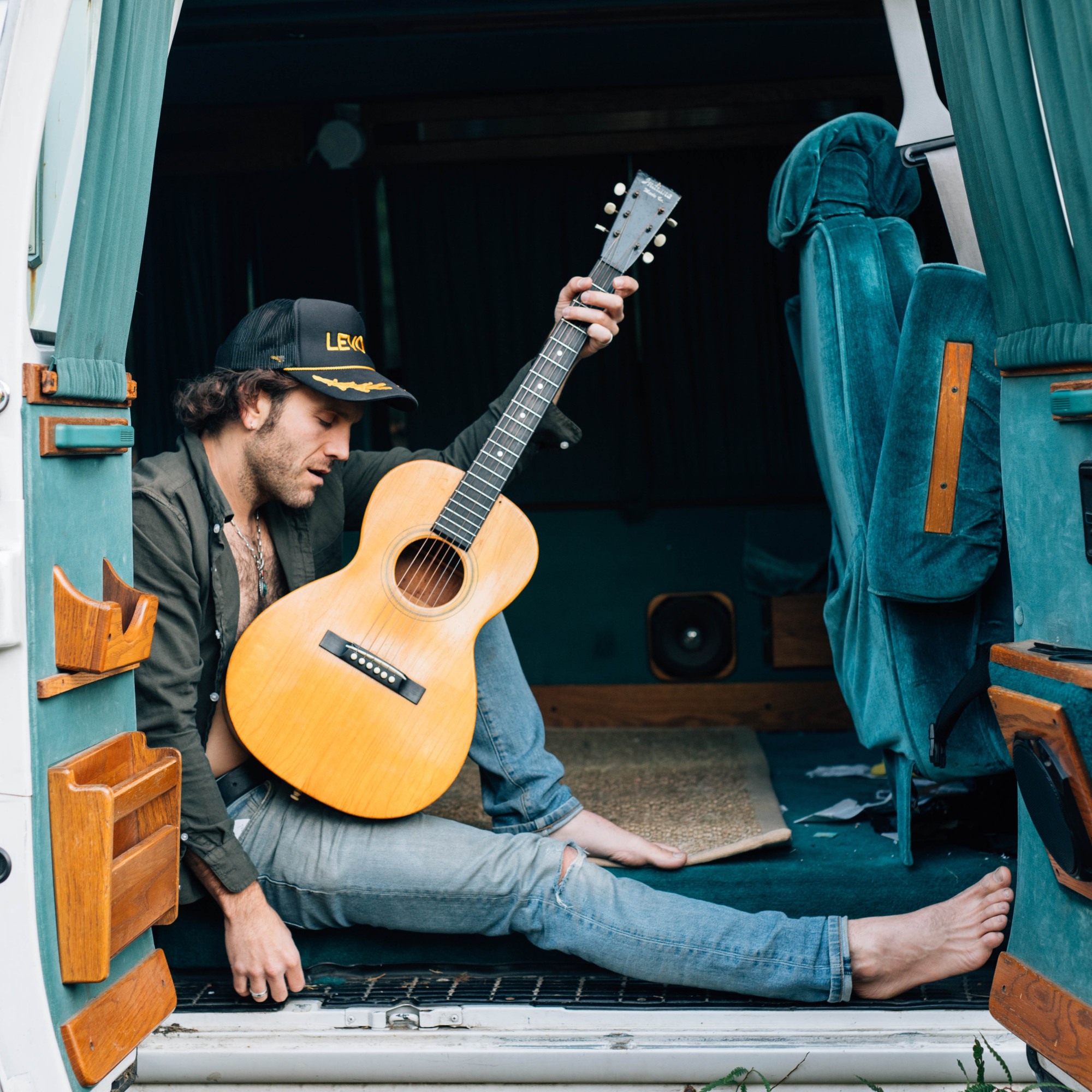 Theo Katzman sitting in a van with a guitar