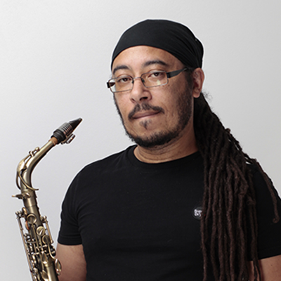 Simon Lee wearing a black t-shirt and glasses, holding a saxophone.