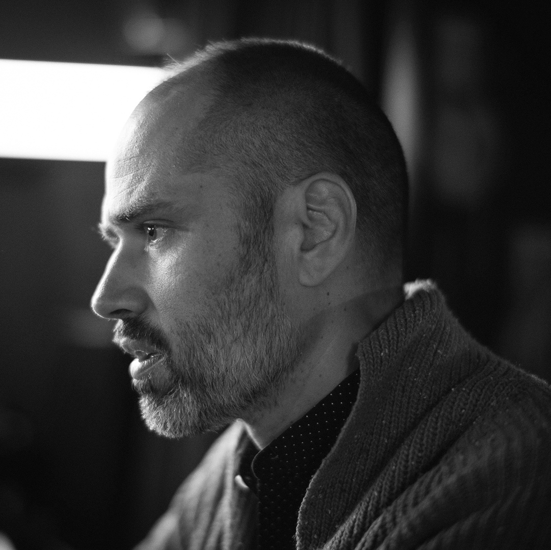 A black and white studio portrait of william brittelle playing a synthesizer in a creative workspace