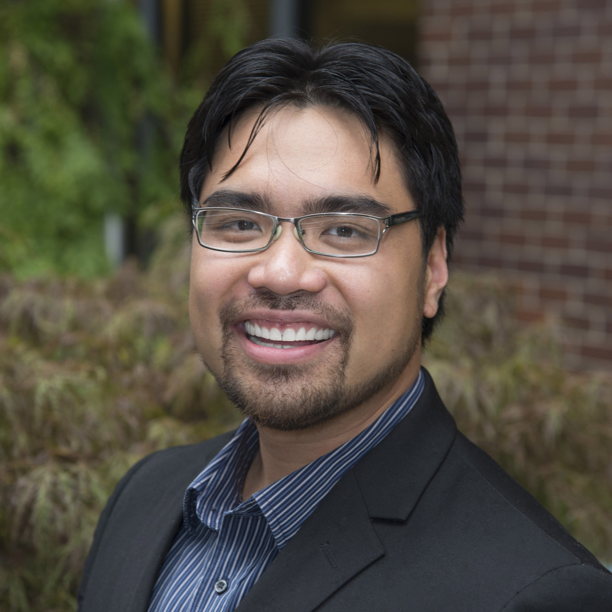 A headshot of a smiling man named Edrex Fontanilla, who is wearing glasses and a business casual outfit, including a black blazer and a blue striped shirt.