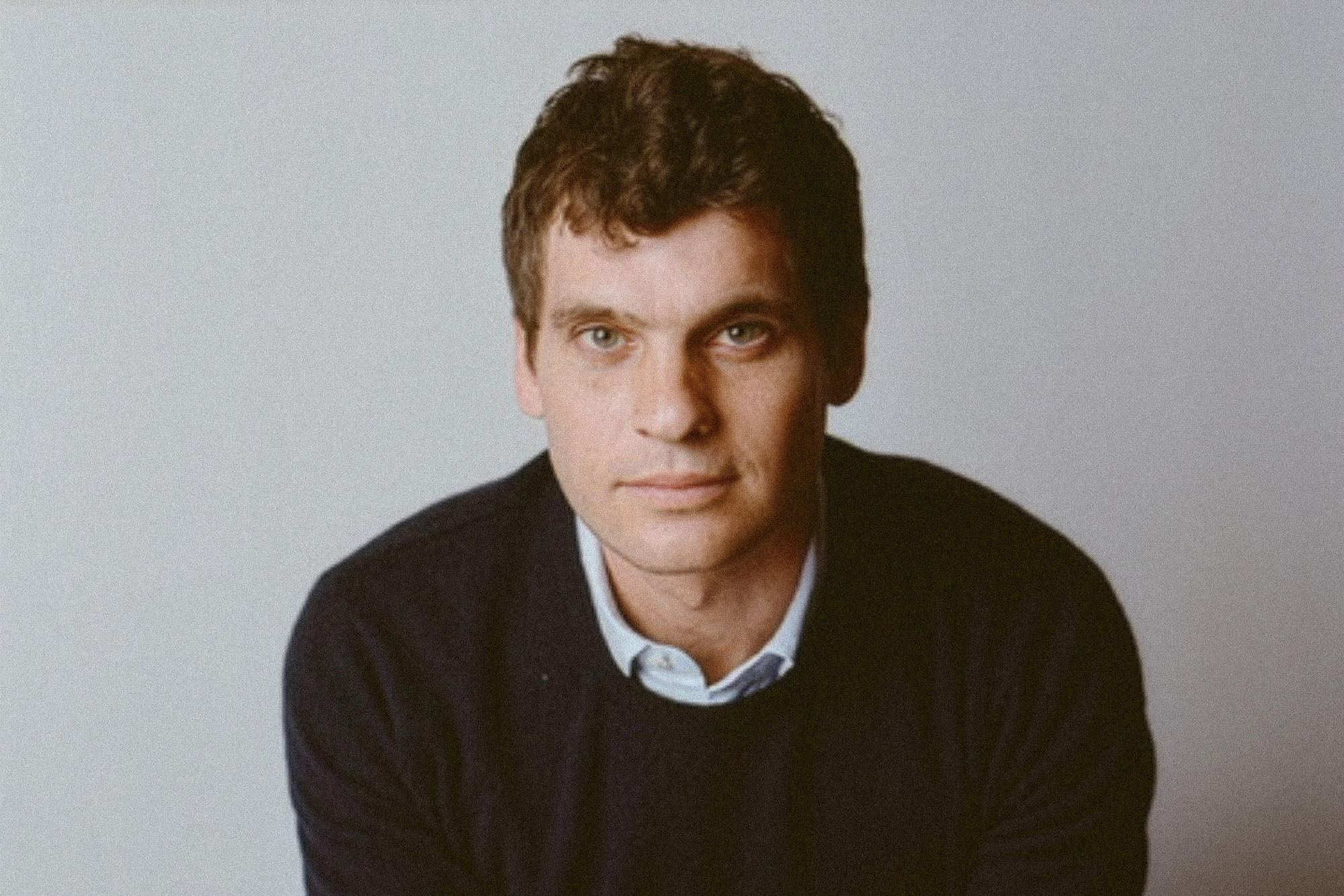 Headshot of a man wearing a button down beneath a dark sweater