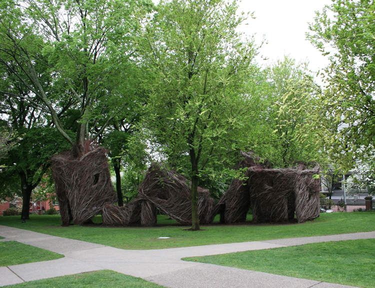 large outdoor sculpture of woven branches on a sunny lawn