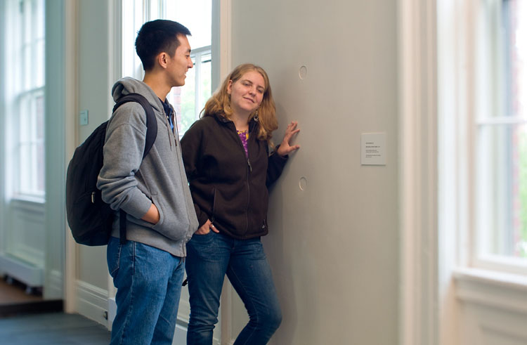 two students listening to audio installation in wall