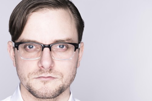 A headshot of Sydney Skybetter. He is a white man with a beard, glasses, brownish-blond hair. He is wearing a white shirt.