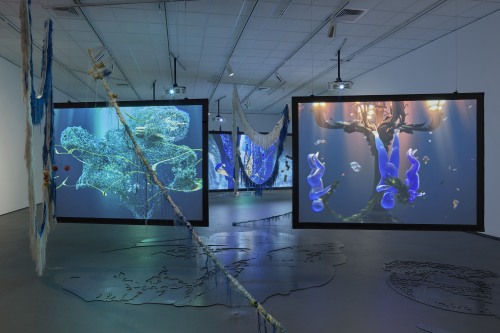 A gallery installation view with two large screens showing underwater animations.