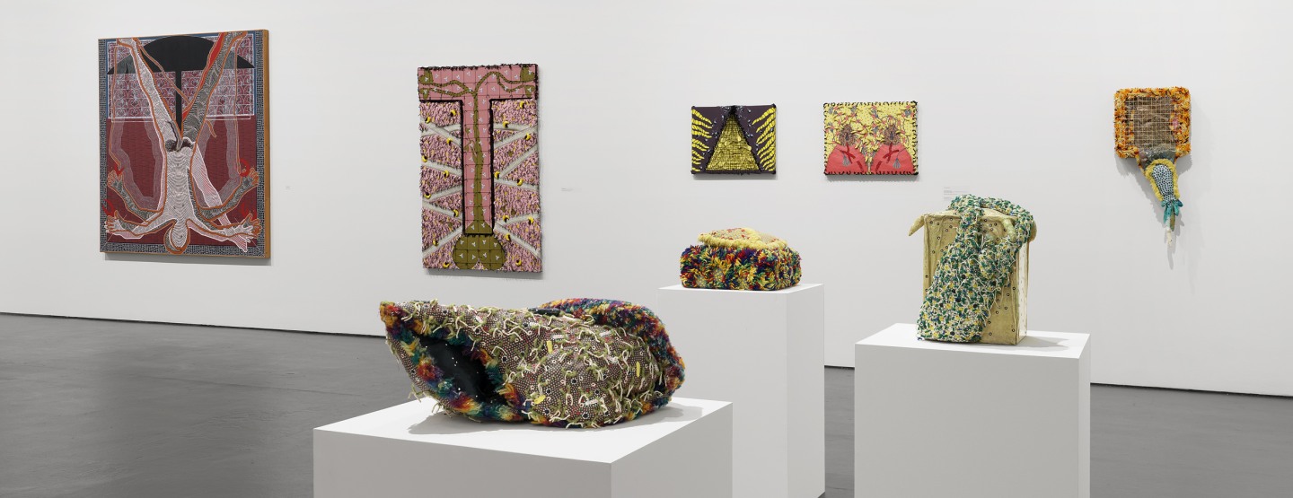 three colorful Franklin Williams sculptural works on white pedestals with five canvas works on the wall behind
