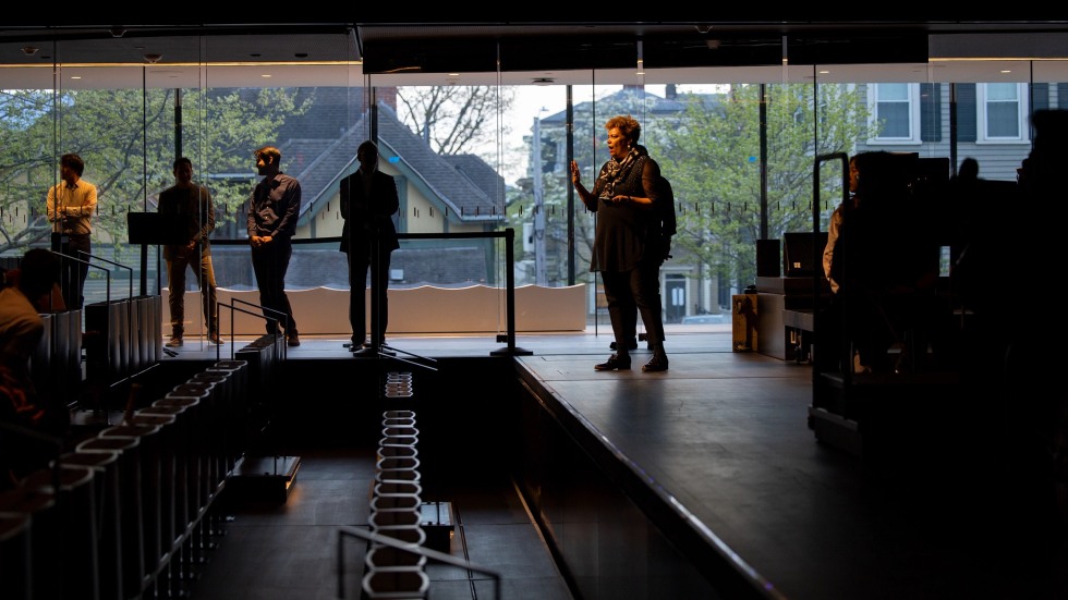 Five silhouetted people in the Main Hall of the Lindemann Performing Arts Center, standing in front of a glass windowed wall.