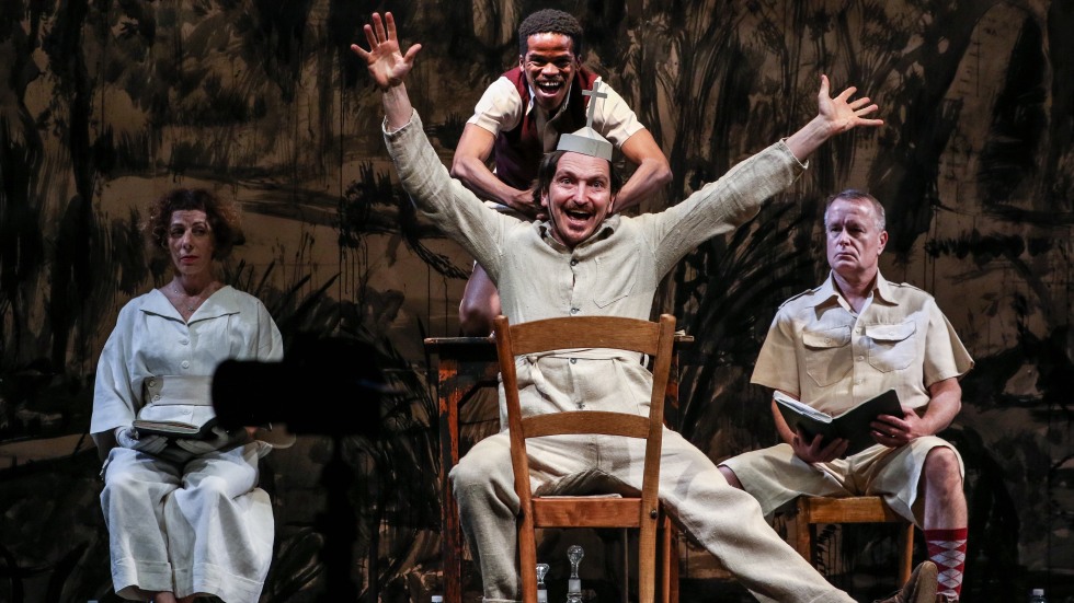 Houseboy show photo. A man sits on a backwards chair while another stands behind him