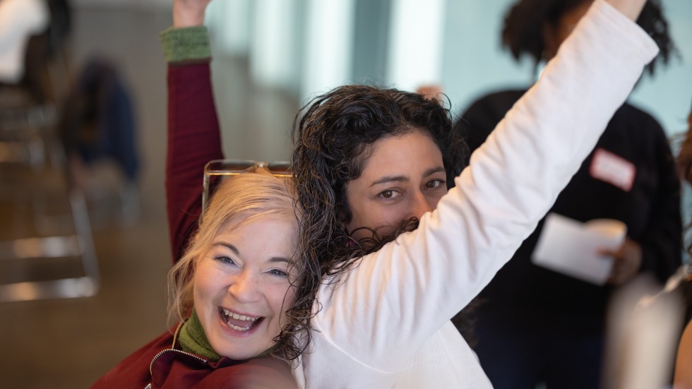 Two women back to back lifting up their arms