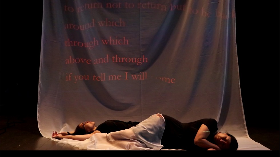 Bonnie and Mary-Kim lying on white fabric with red text projected on surface. 