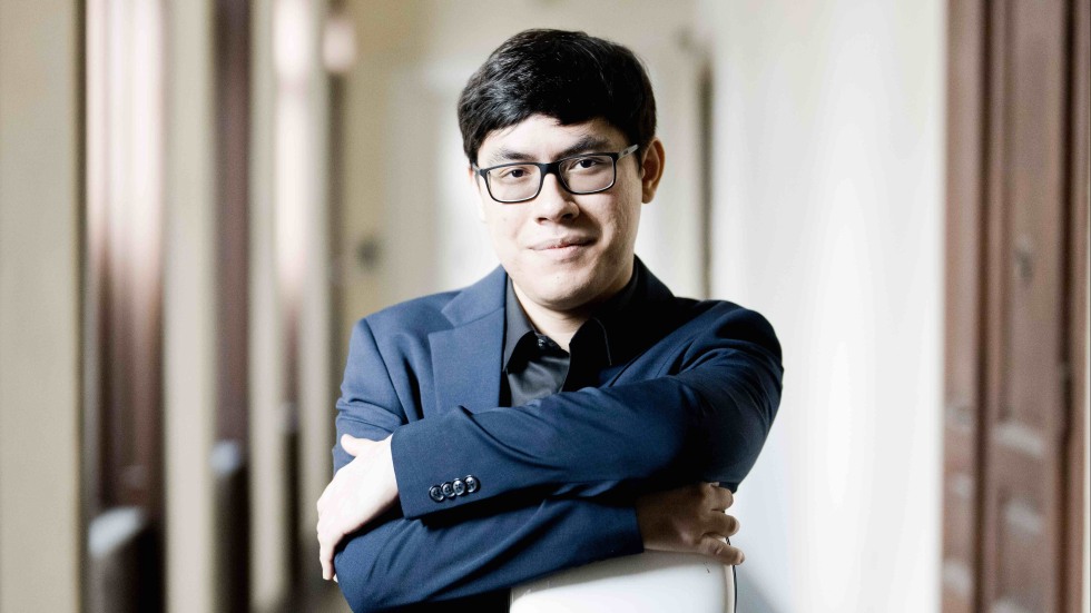 Zlatomir Fung standing in a hallways leaning on a white cello case