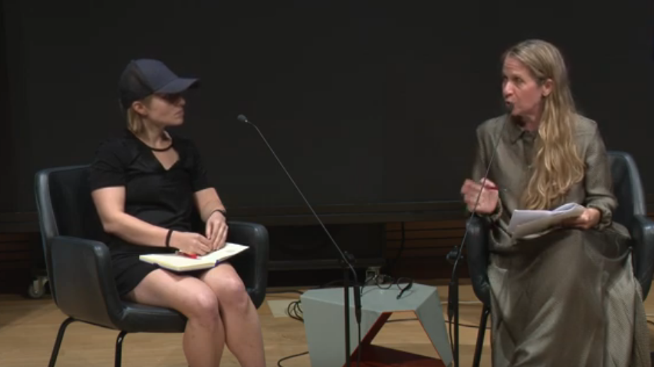 Two women seated on a stage in a panel set up.