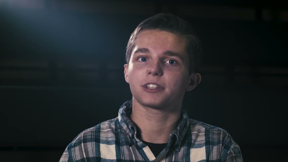 A student looking in a black background with light coming over his shoulder.