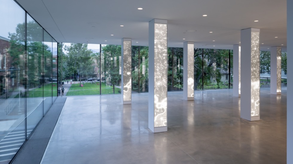 illuminated columns with abstract light patterns inside a glass-walled gallery during daytime